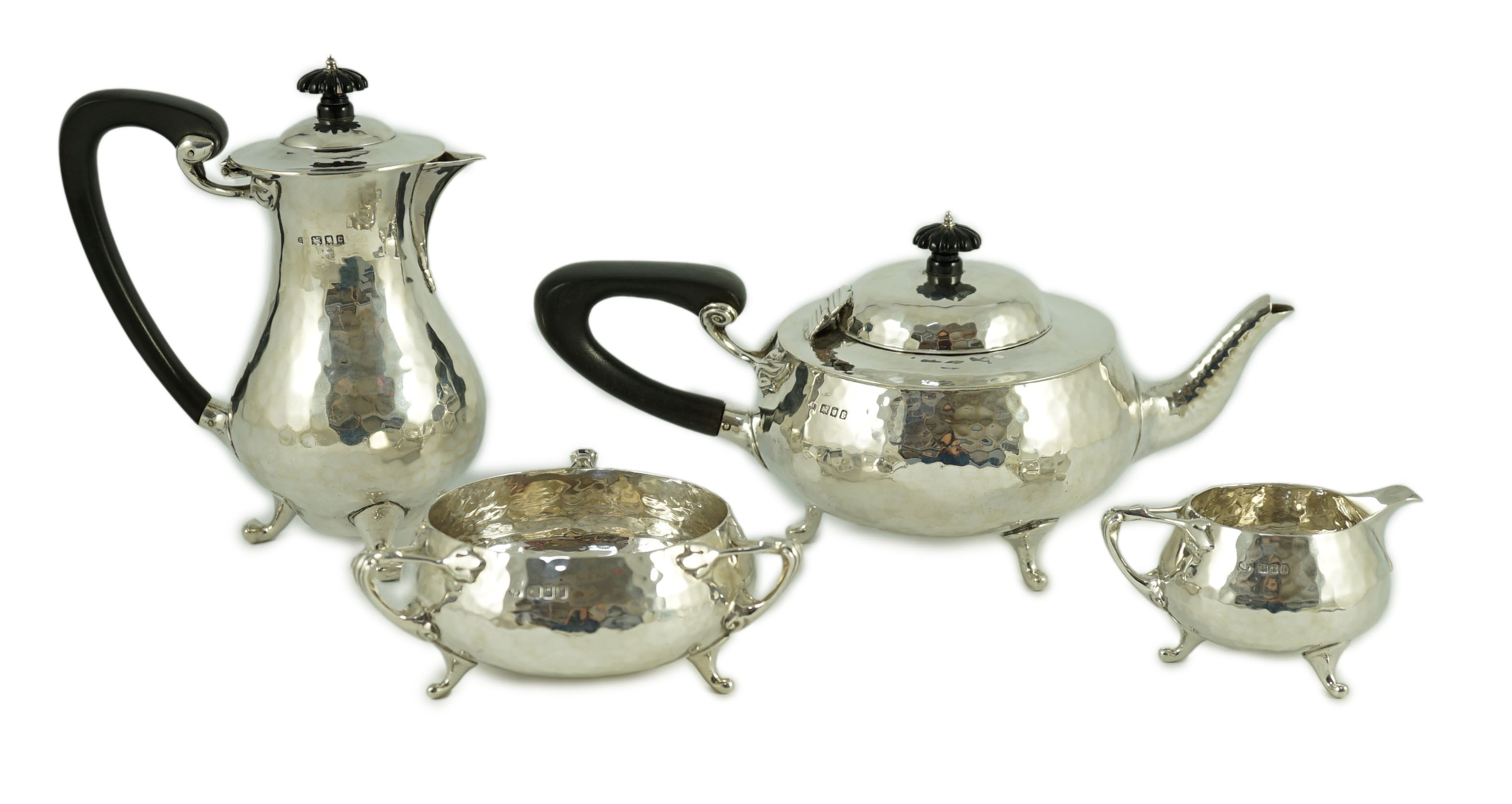 A George V Arts and Crafts three piece planished silver tea set and a similar hot water pot, by Charles Edwards